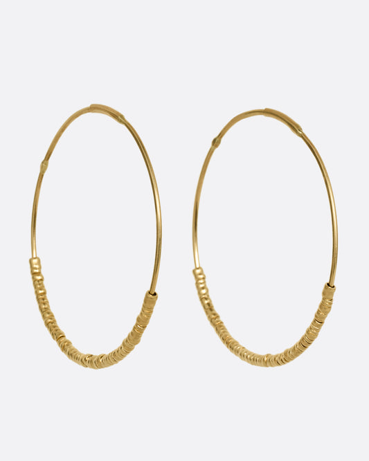 A pair of yellow gold hoop earrings with freely moving beads. Shown at an angle from the front.
