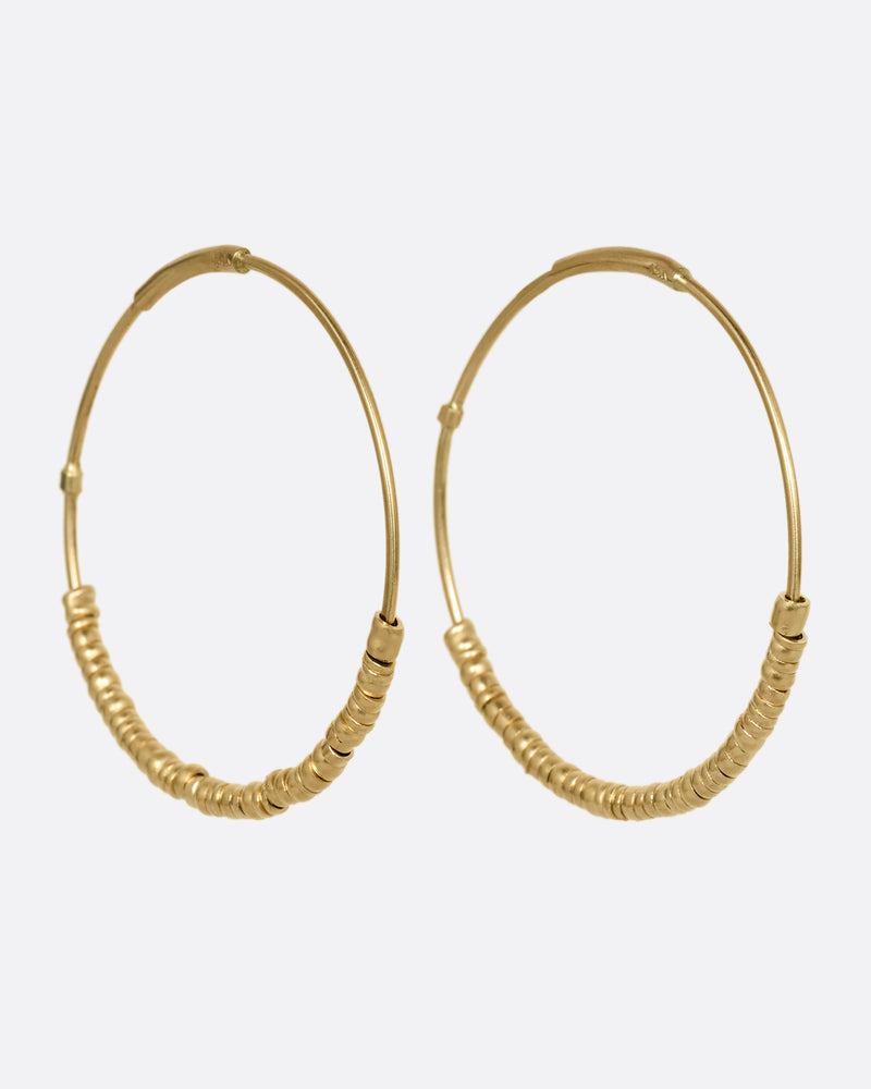 A pair of yellow gold hoop earrings with freely moving beads. Shown at an angle from the front.