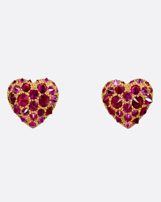A pair of yellow gold heart shaped stud earrings with reverse set rubies of varying sizes set into them. Shown from the front.