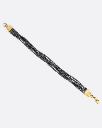A bracelet with five strands of oxidized silver beads converging at  yellow gold capped ends with a lobster clasp. Shown open from the top.
