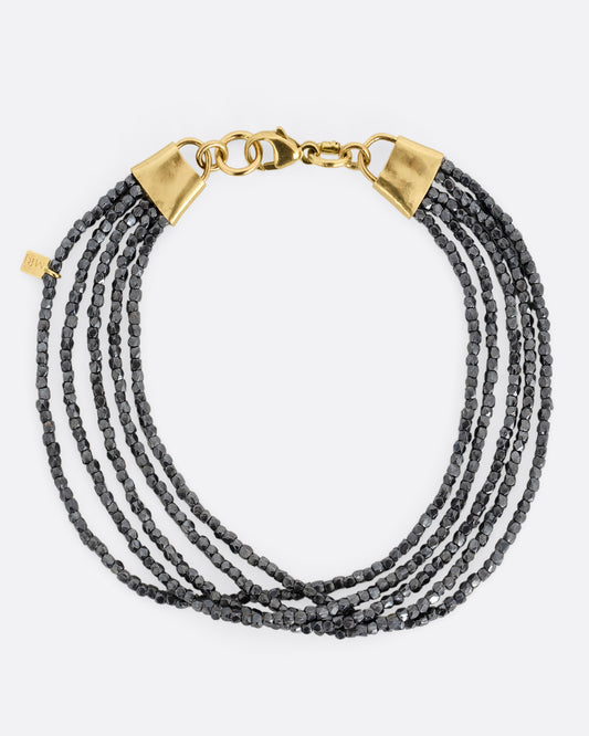 A bracelet with five strands of oxidized silver beads converging at  yellow gold capped ends with a lobster clasp. Shown from the top.