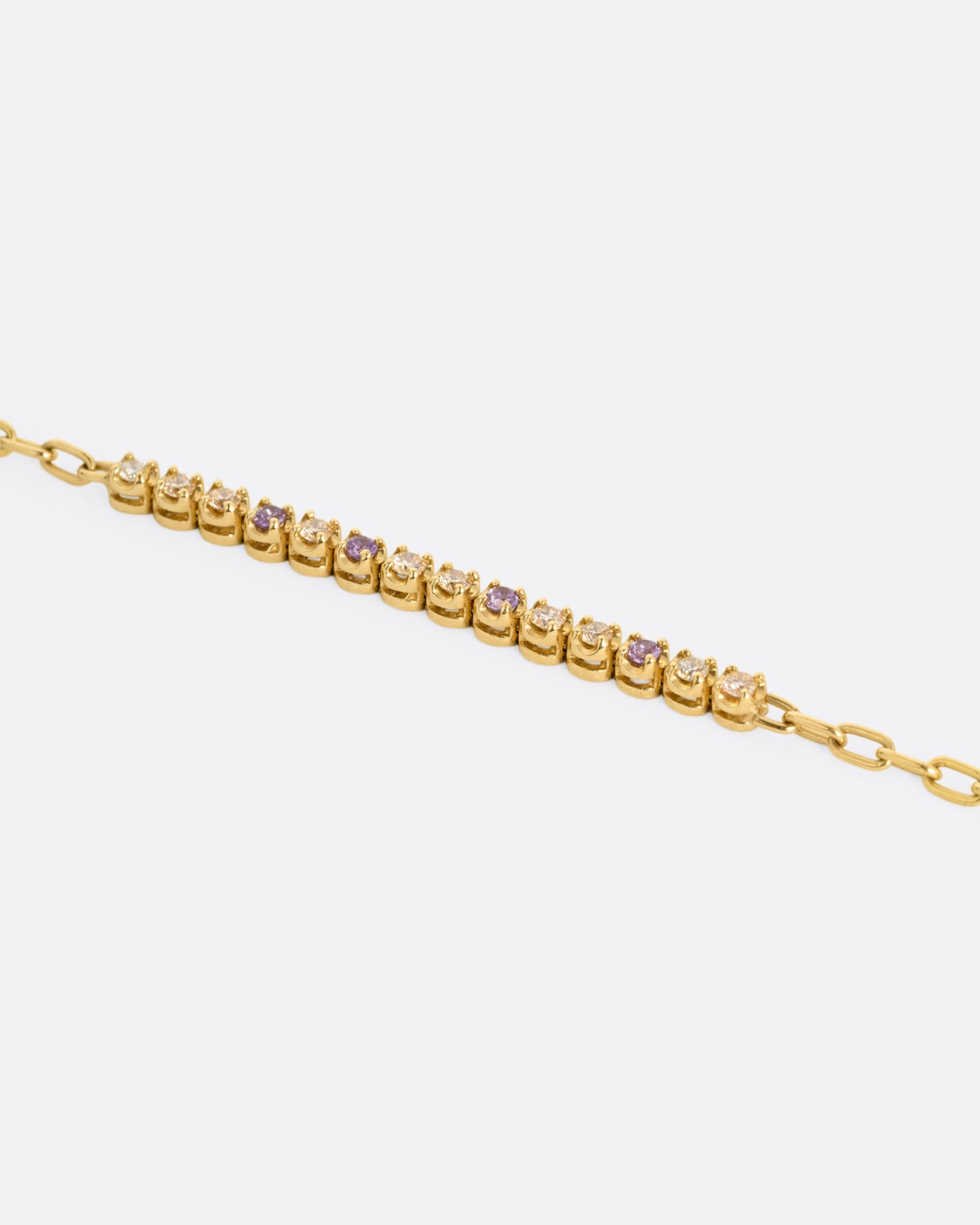 A close up of a yellow gold partial tennis bracelet with peach and yellow diamonds and purple sapphires. 