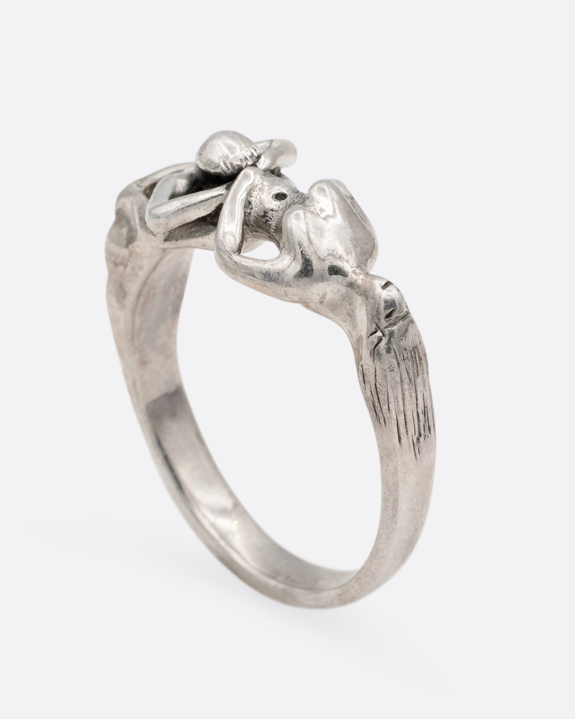 A silver ring with an erotic couple. Shown standing from the side.