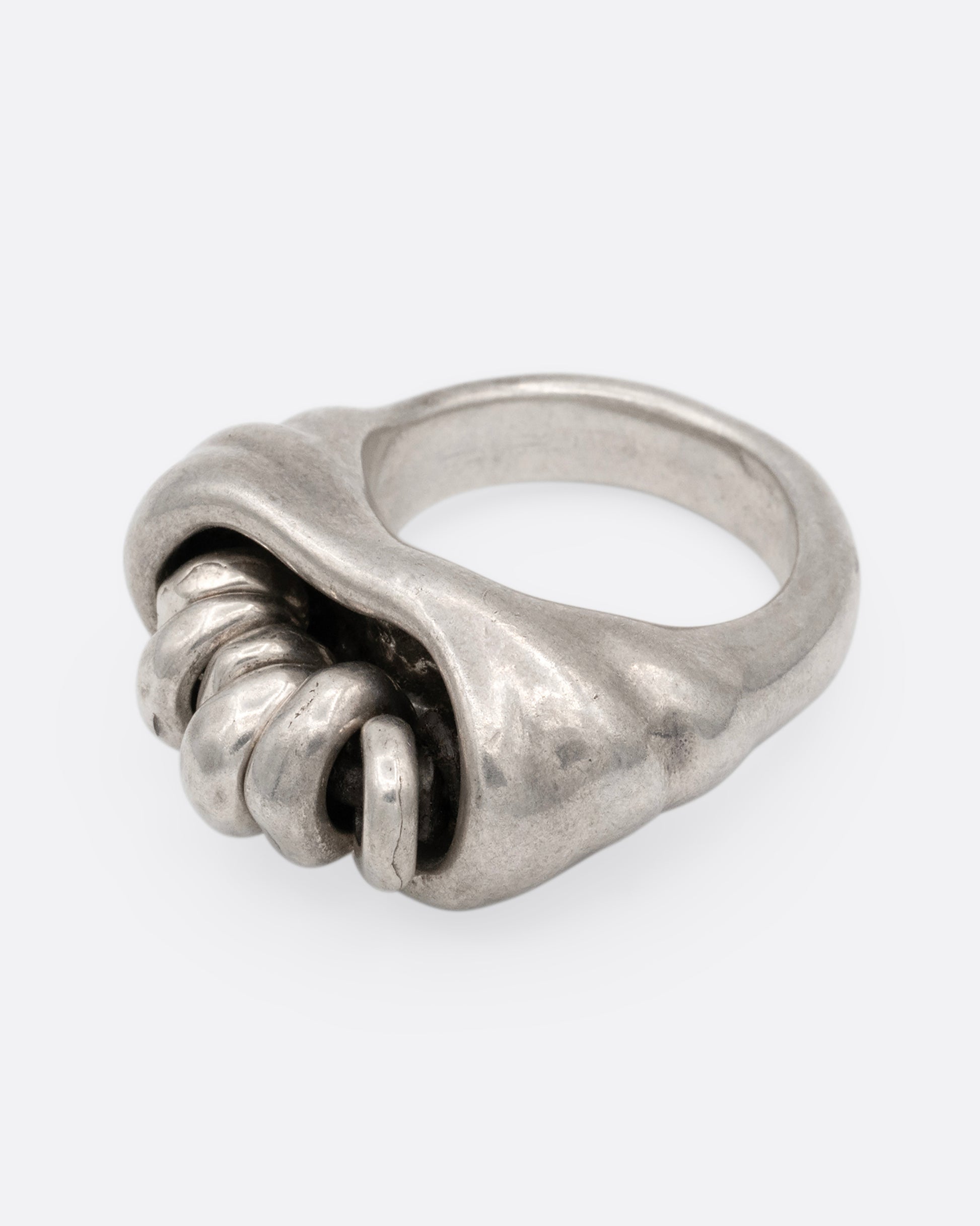 A silver ring with a cluster of free moving hoops nestled into its towering face. Shown from the side.