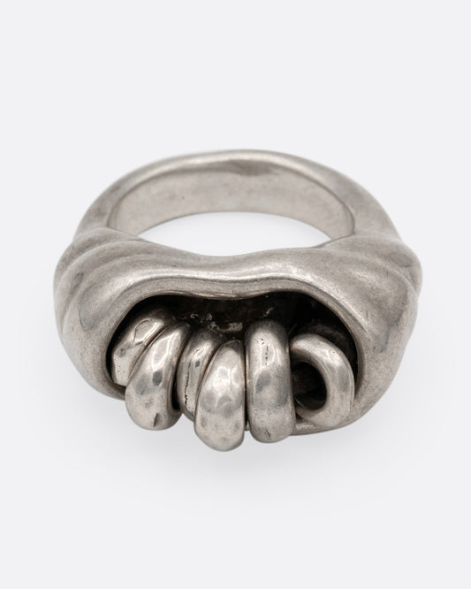 A silver ring with a cluster of free moving hoops nestled into its towering face. Shown from the front.