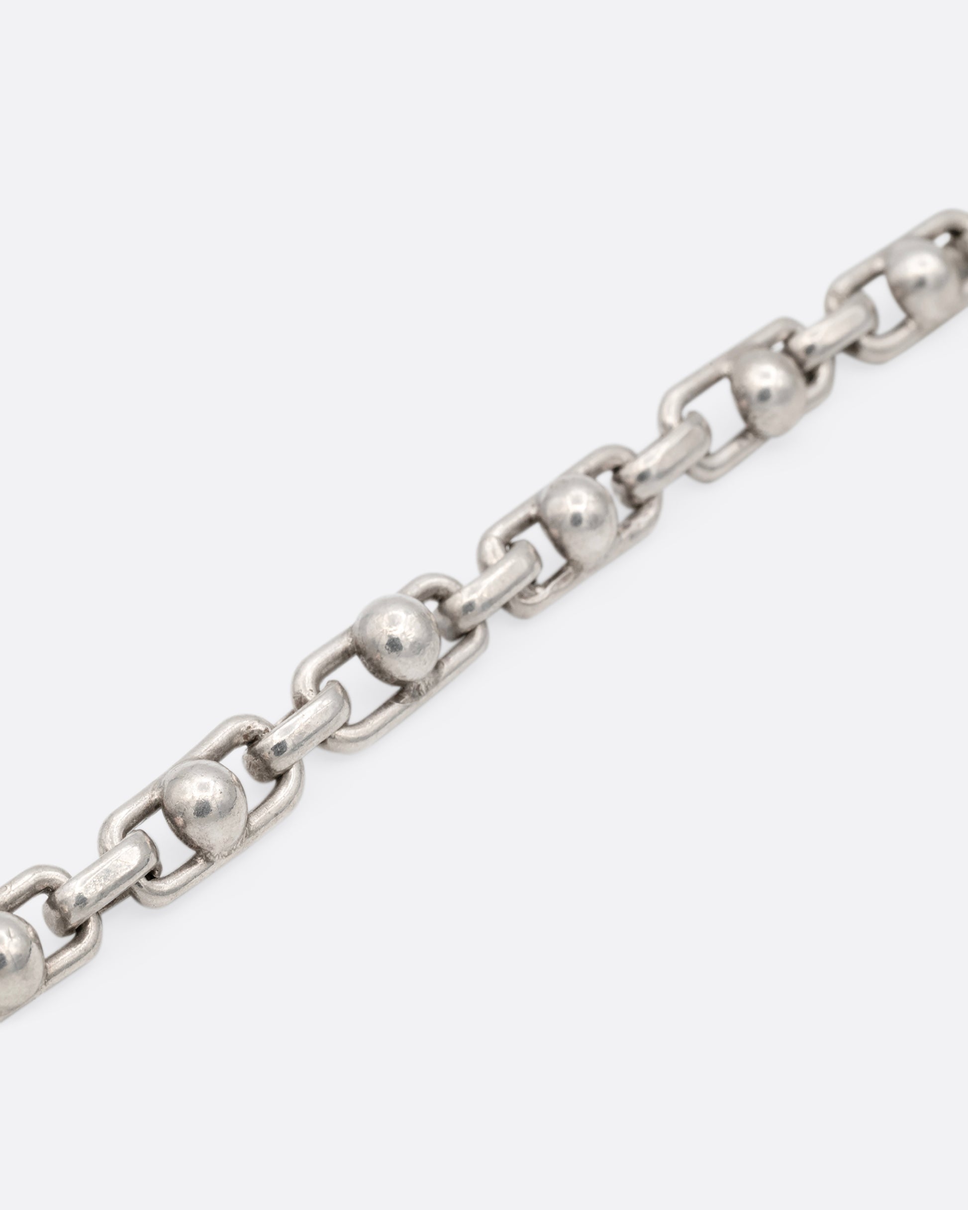 A close up of a silver bracelet with spheres at the center of each link. 