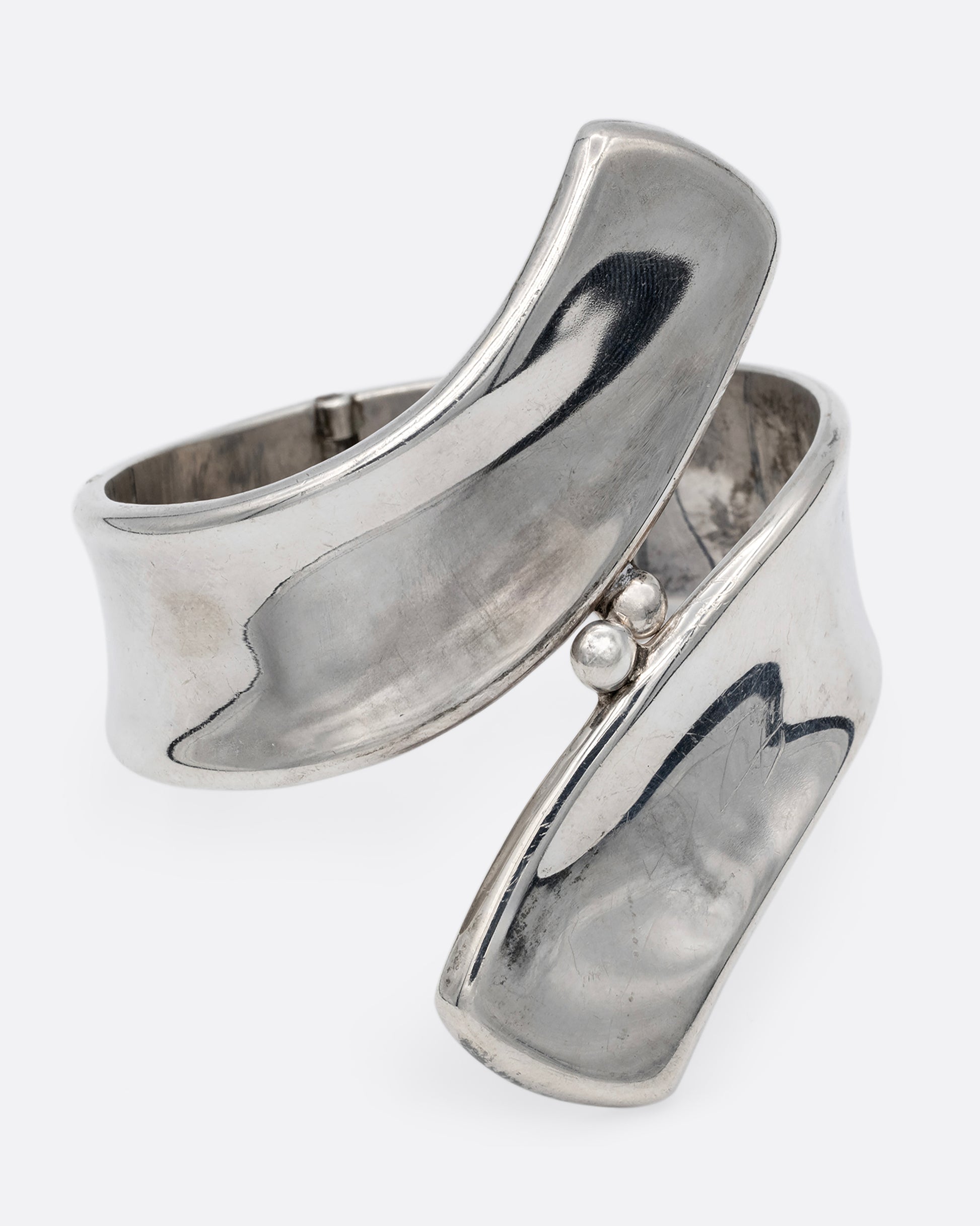A silver ribbon shaped hinged cuff bracelet in a loop shape. Shown from the front.