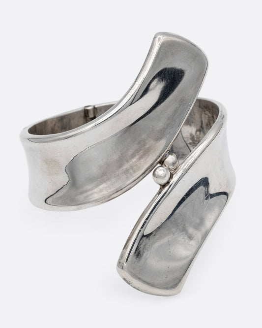 A silver ribbon shaped hinged cuff bracelet in a loop shape. Shown from the front.