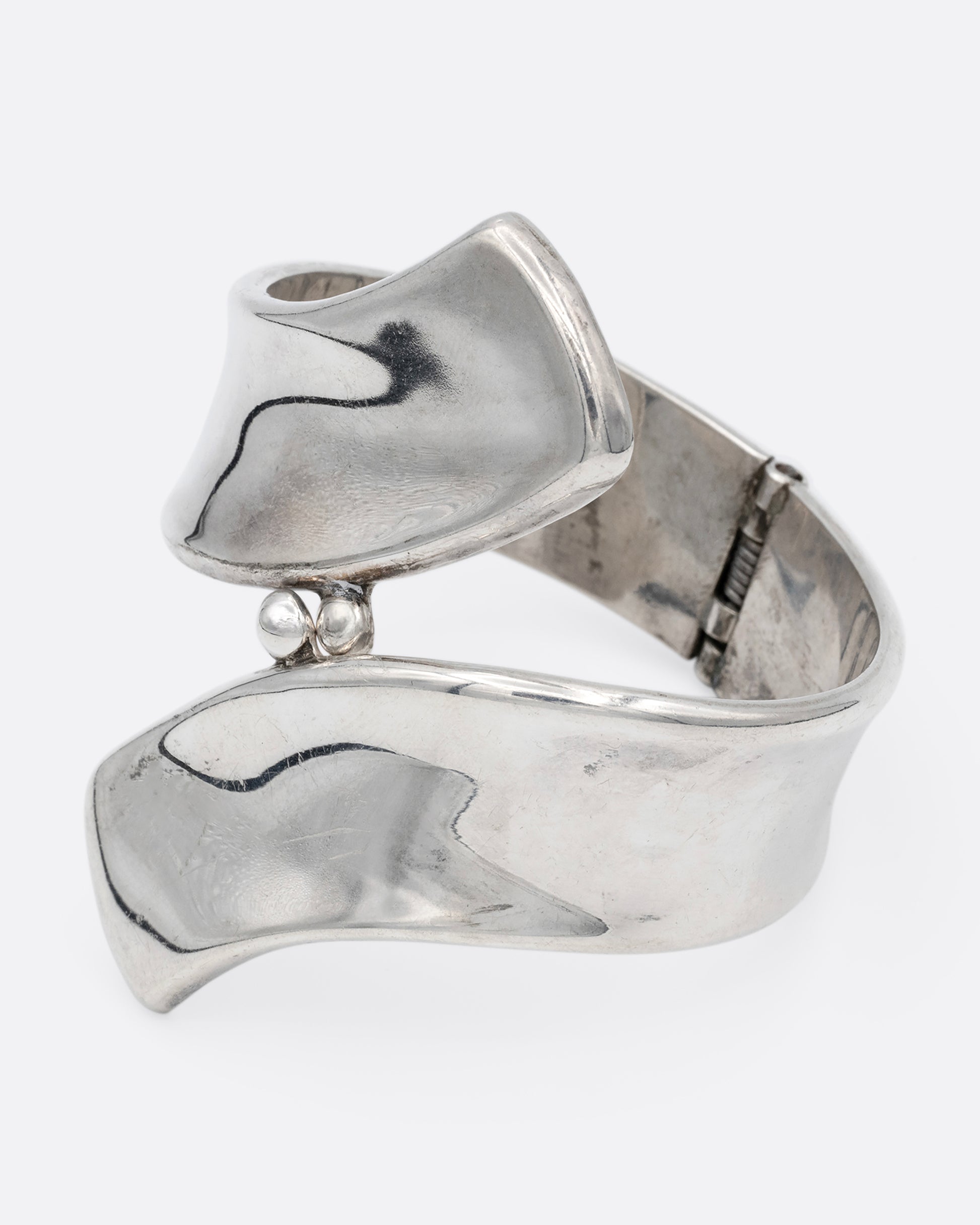 A silver ribbon shaped hinged cuff bracelet in a loop shape. Shown from the side.