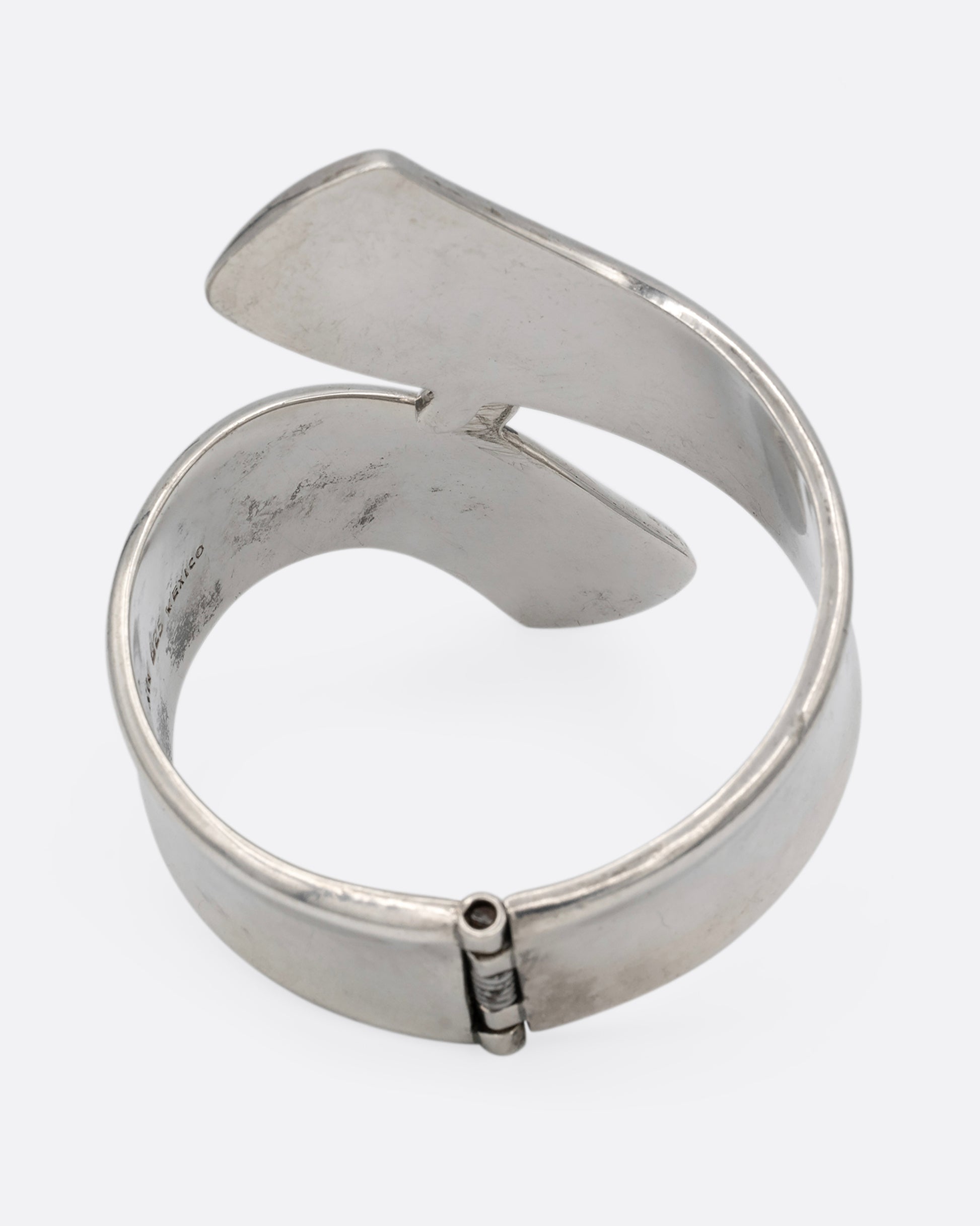 A silver ribbon shaped hinged cuff bracelet in a loop shape. Shown from the back.