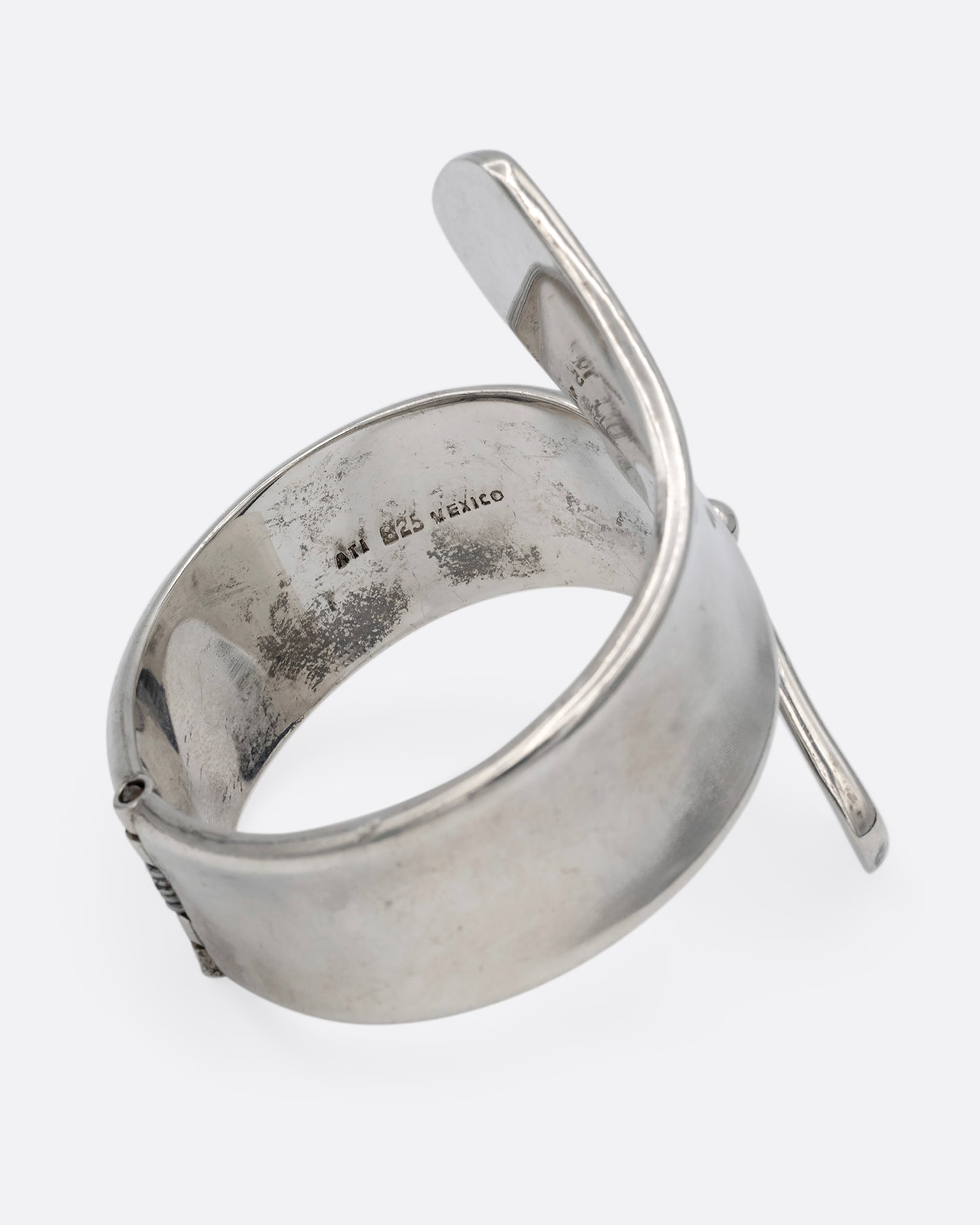 A silver ribbon shaped hinged cuff bracelet in a loop shape. Shown from the side.