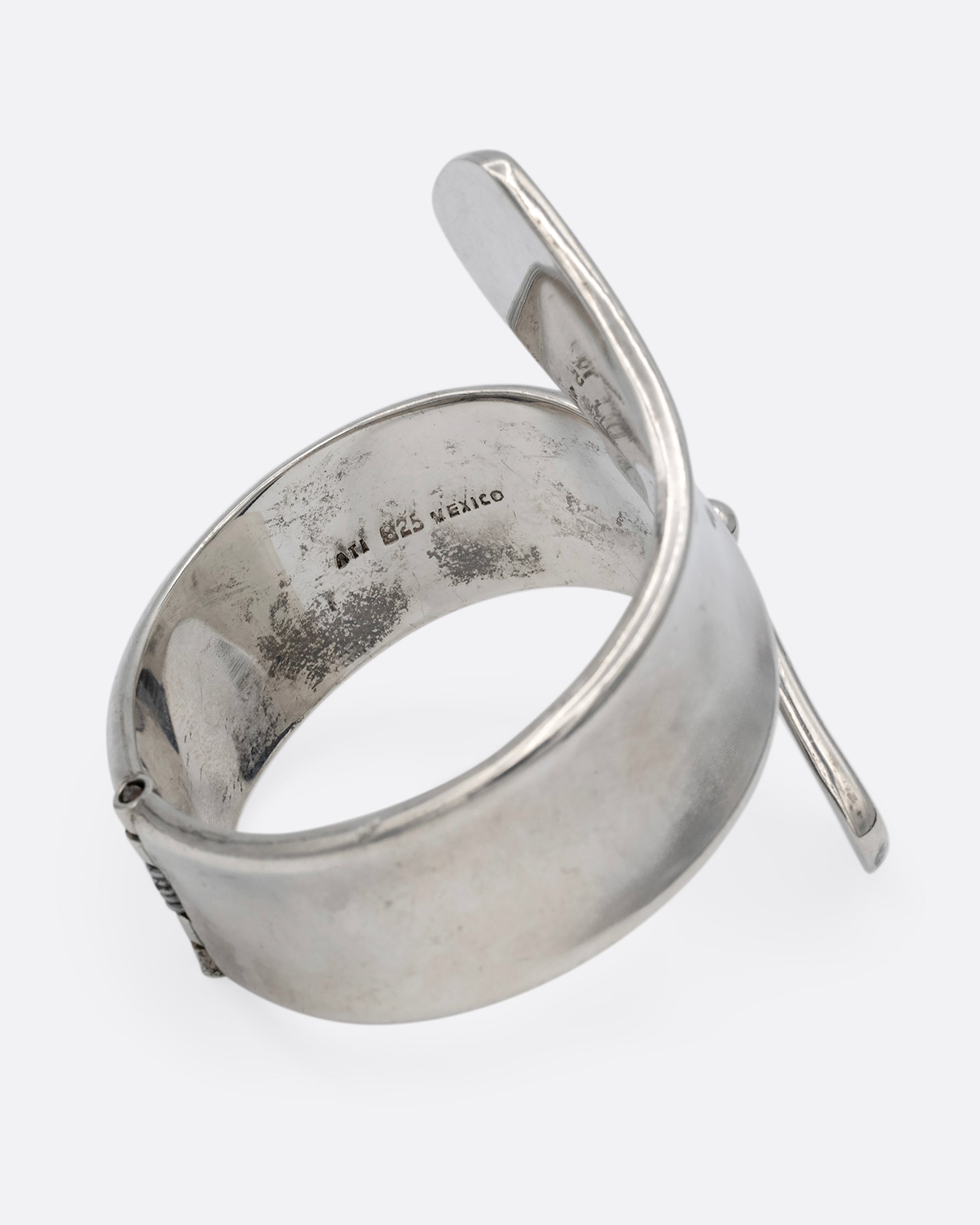 A silver ribbon shaped hinged cuff bracelet in a loop shape. Shown from the side.