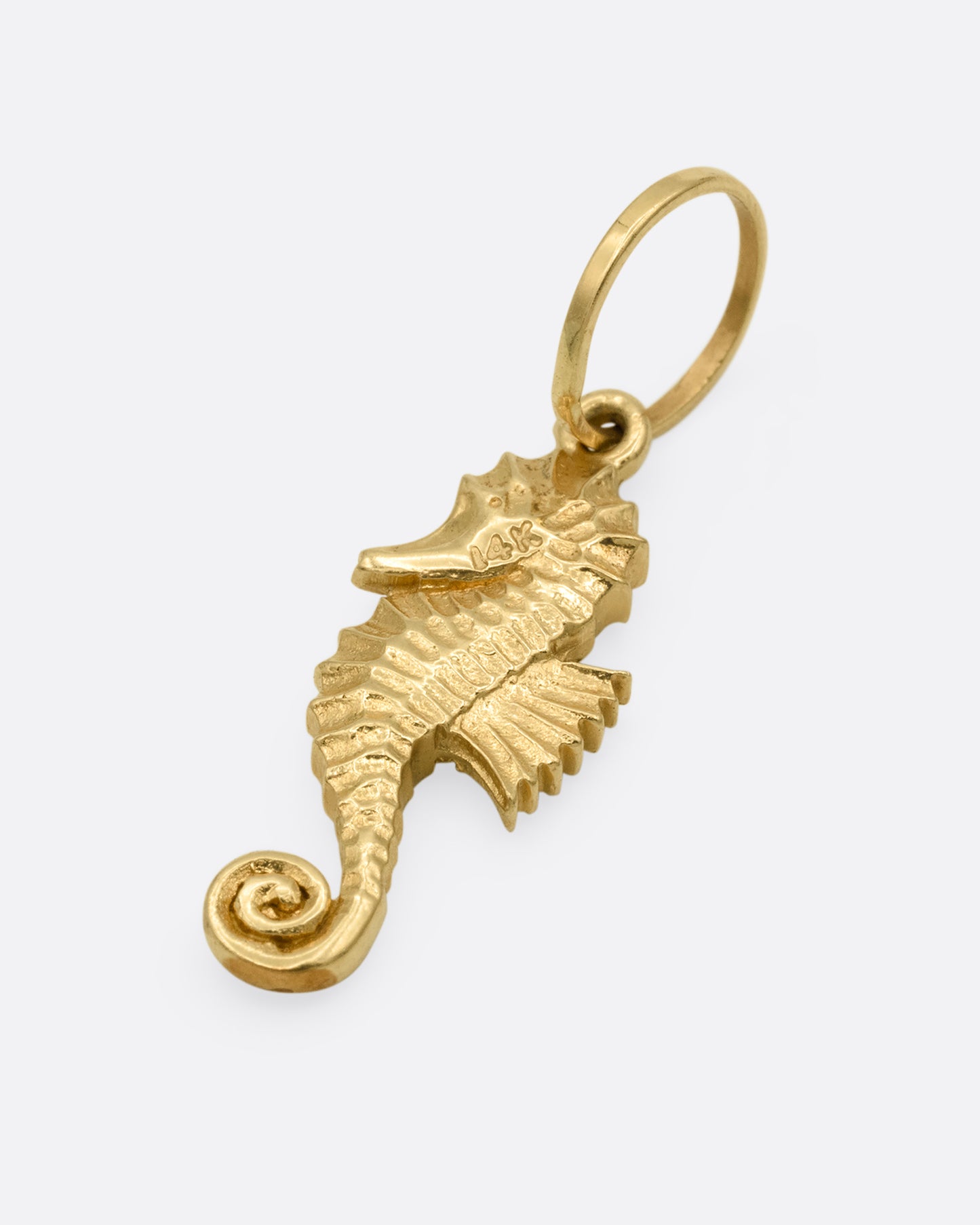A yellow gold seahorse charm. Shown lying flat from the front.