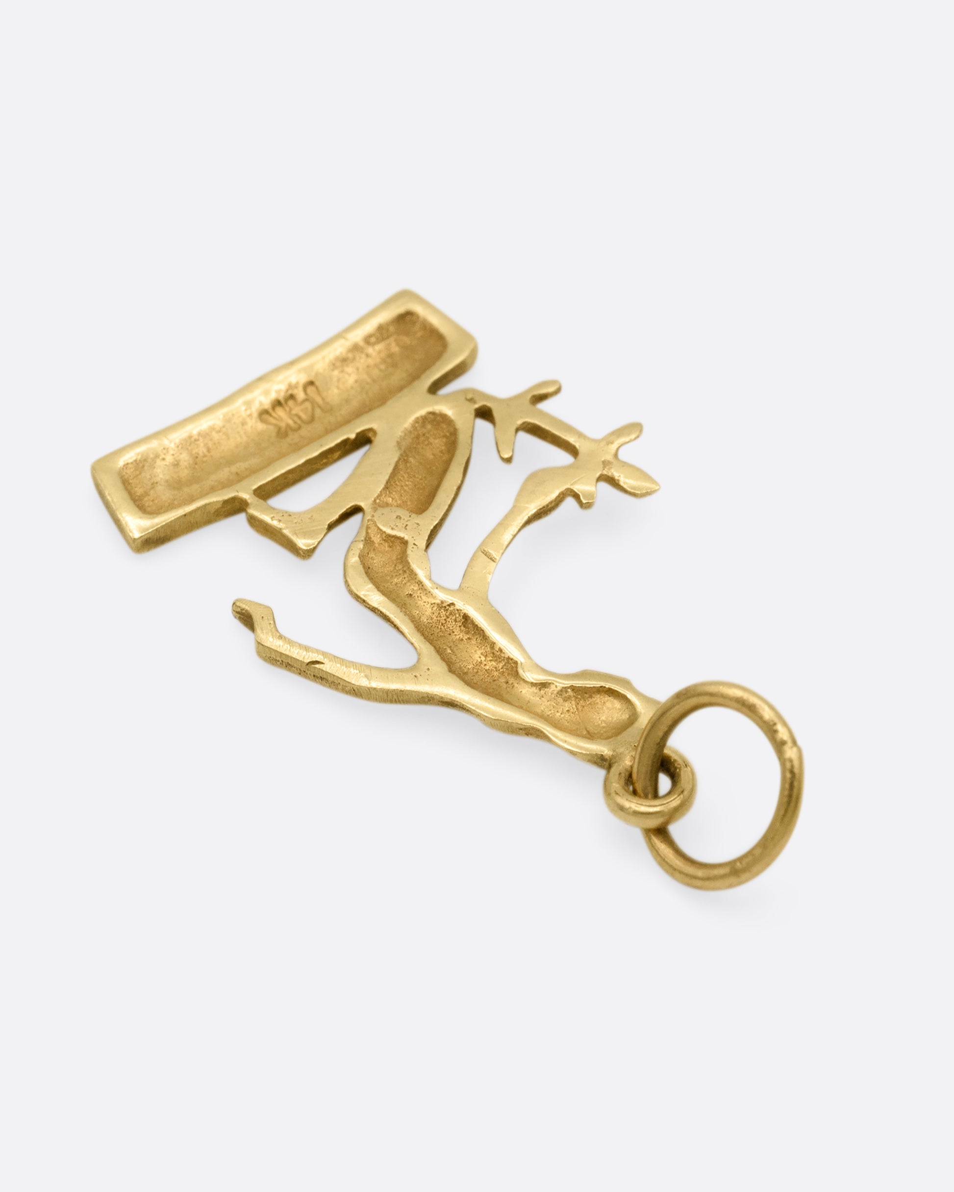 A yellow gold kneeling Virgo charm, depicted carrying a sheaf of wheat. Shown from the back.