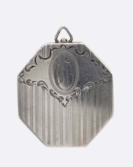 An octagonal silver locket with intricate stripe engravings and a scrolling letter 'C'. Shown from the front.
