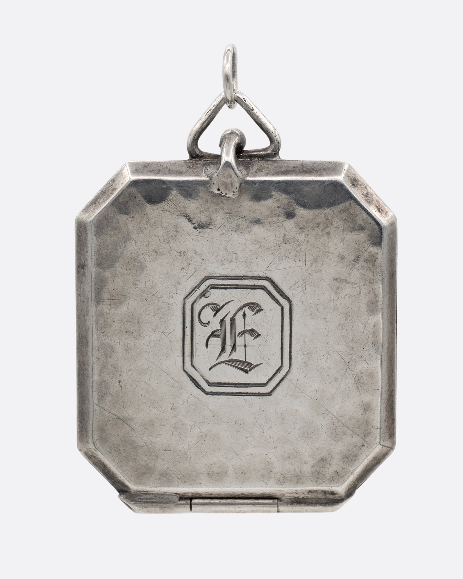 A silver octagonal locket with an 'E' engraved a its center. Shown from the front.