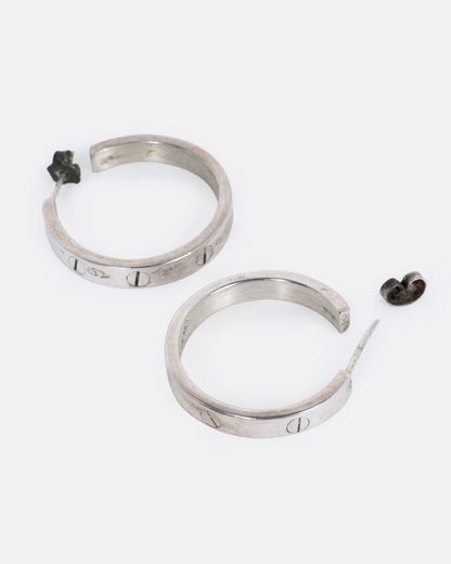 A pair of silver hoop earrings with a motif mimicking flat head screws, shown from the side with one earring open.