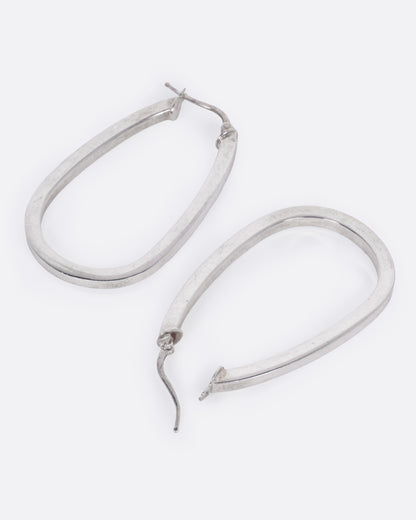 A pair of silver hoop earrings with a squared edge and oval shape, shown from the side with one earring open.