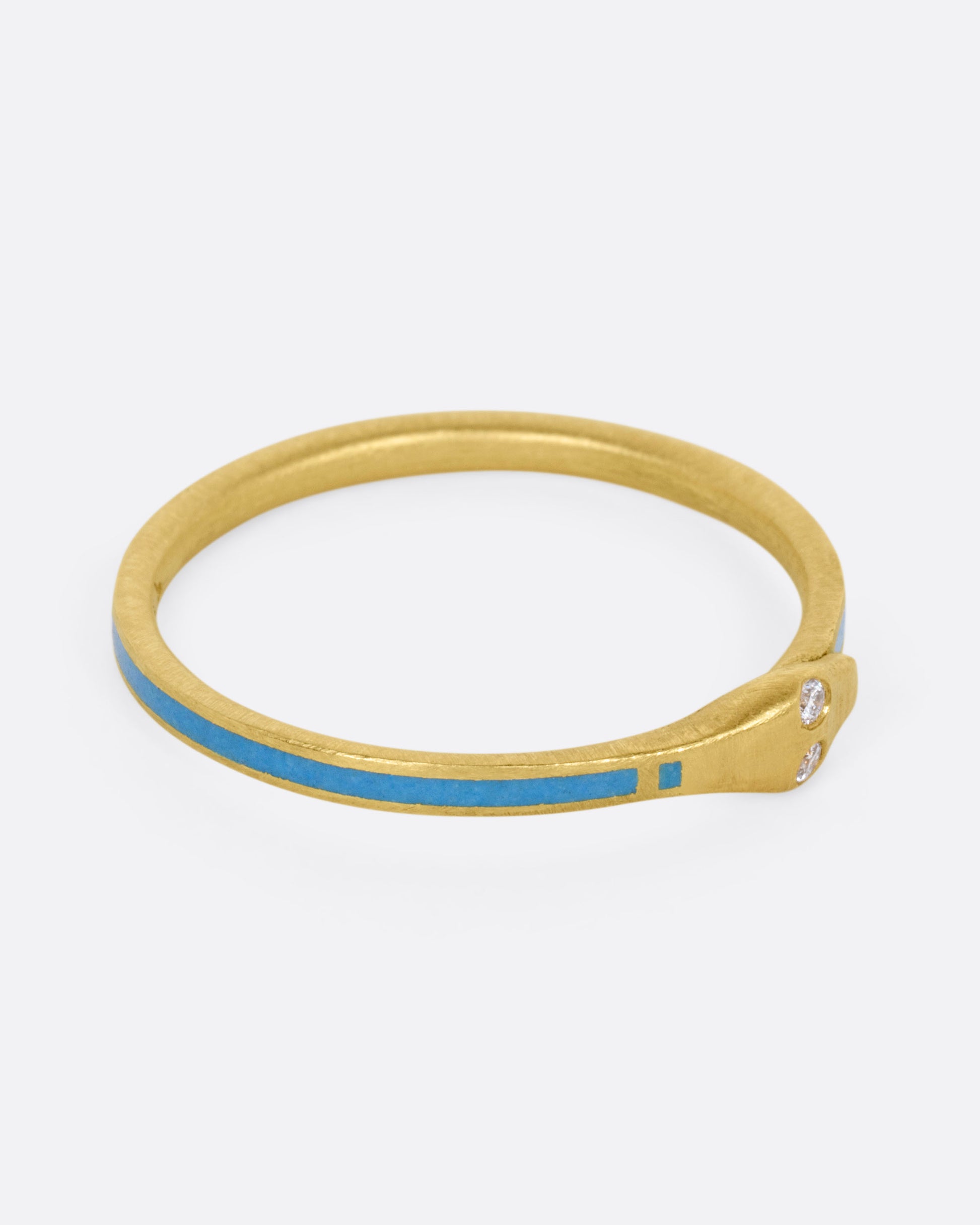 A yellow gold ouroboros ring with diamond eyes and pale blue enamel, shown from the side. 