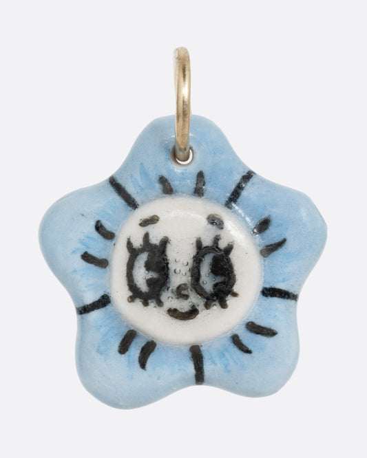 A blue flower porcelain flower charm with a face at the center. Shown from the front.