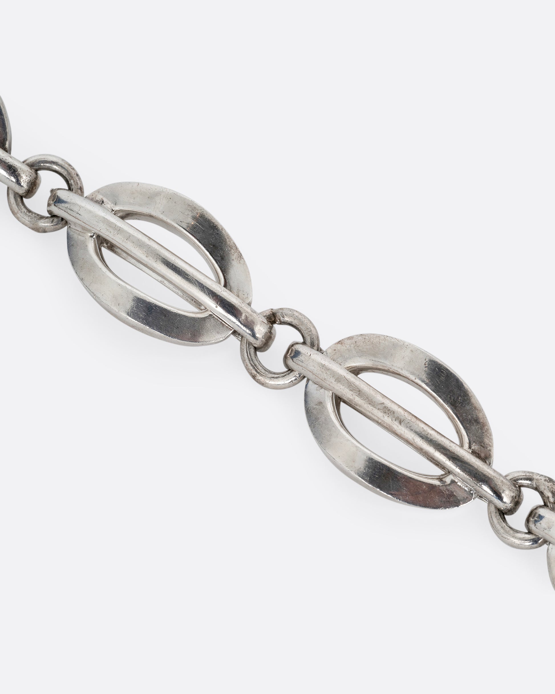 A close up of a silver split oval link bracelet. Shown open lying flat.