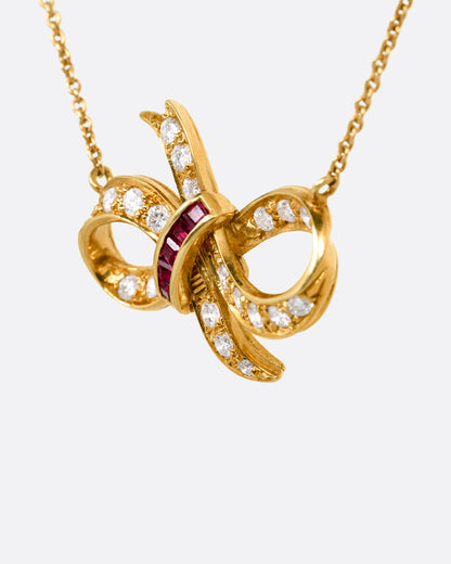 A yellow gold cable chain necklace with a diamond and ruby studded bow at the center. Shown from the side.