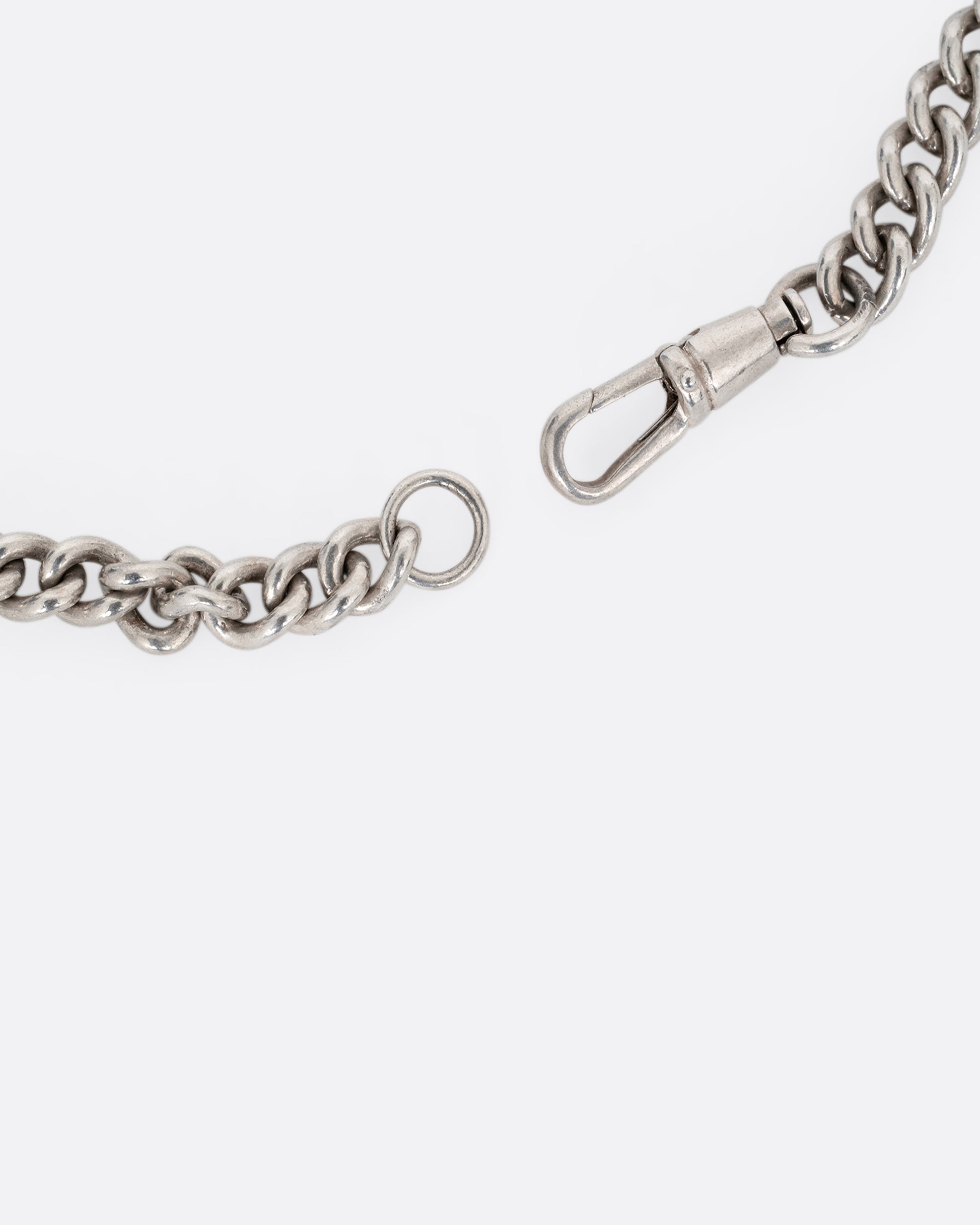 A close up of a silver curb chain pocket watch curb chain necklace with a T-bar on one end. 