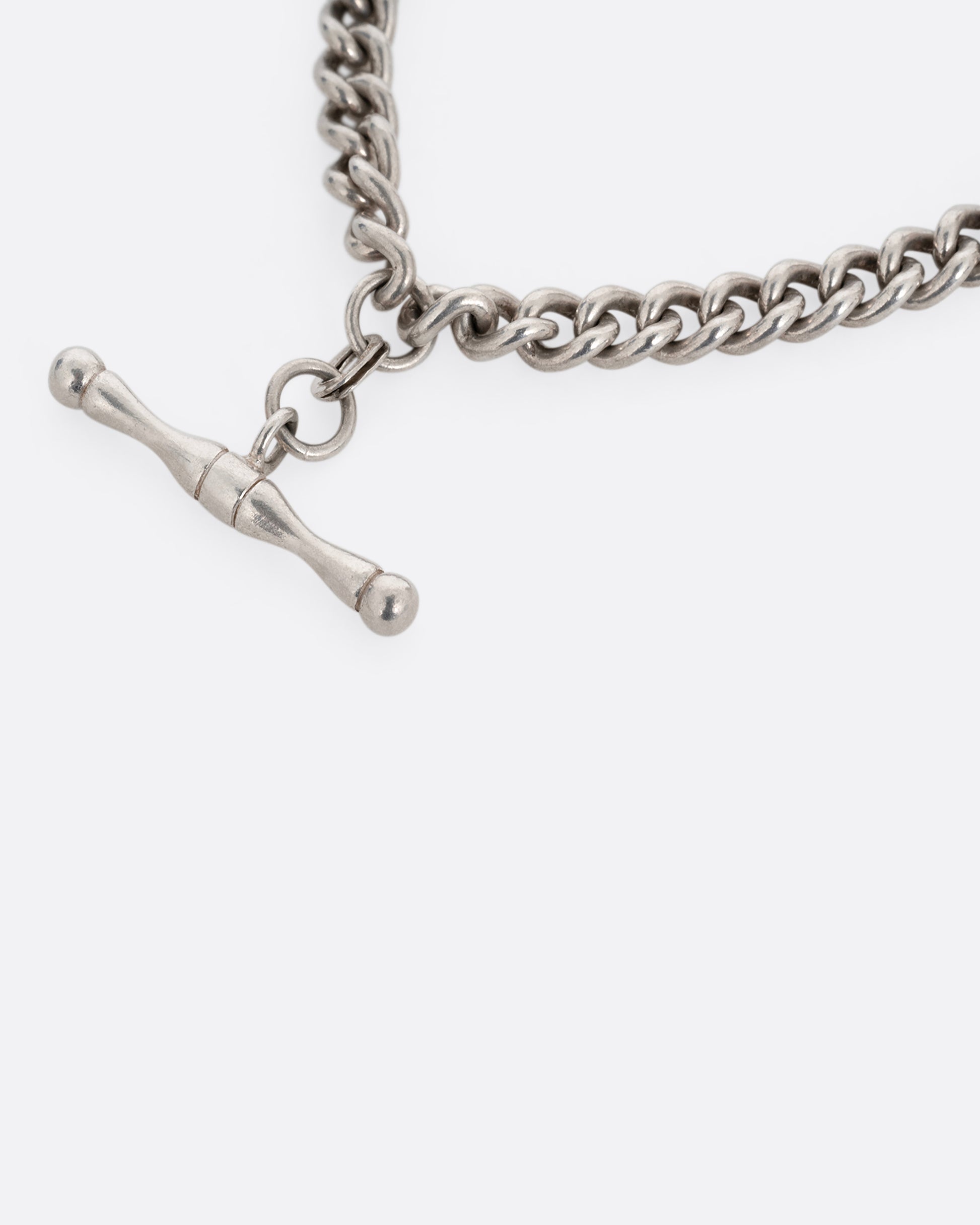 A close up of a silver curb chain pocket watch curb chain necklace with a T-bar on one end. 