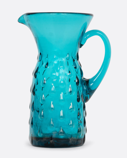 A teal glass creamer with a funnel shaped top, handle, and a bubbly teardrop pattern.  Shown from the side.