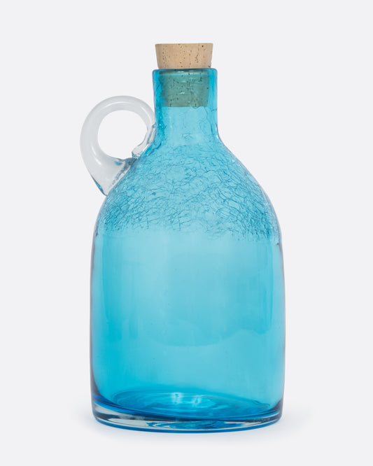 A glass aqua moonshine jug from Blenko with a clear crystal handle, a crackled finish at the top, and a cork stopper. Shown from the side.