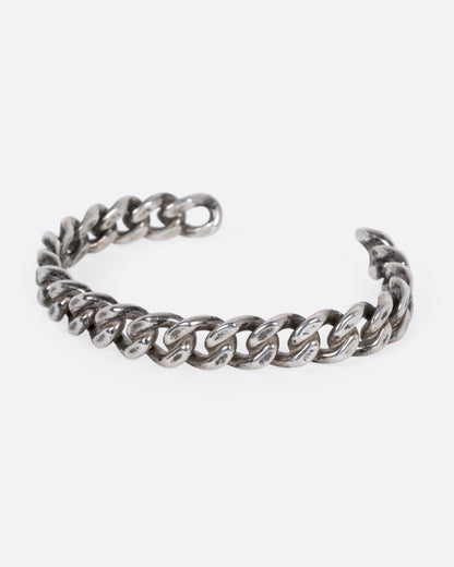 A silver curb chain cuff bracelet shown from the side.