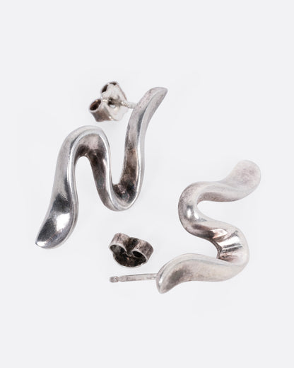 A pair of silver wavy stud earrings shown from the side with one earring open.