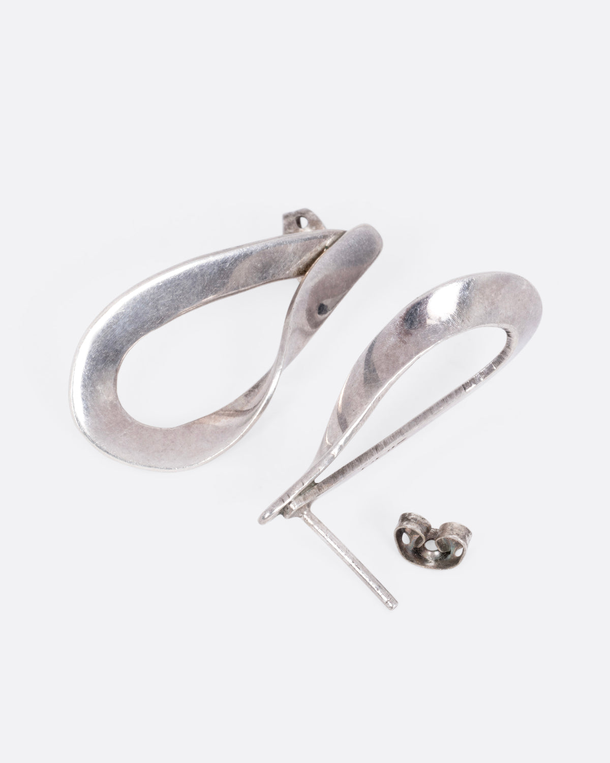 A pair of silver twisted dimensional drop studs, shown from the side with one earring open.