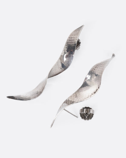 A pair of silver twisty earrings with a hammered finish, shown from the side with one earring open.