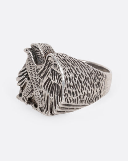 A silver signet ring with a textured eagle design, shown from the side.