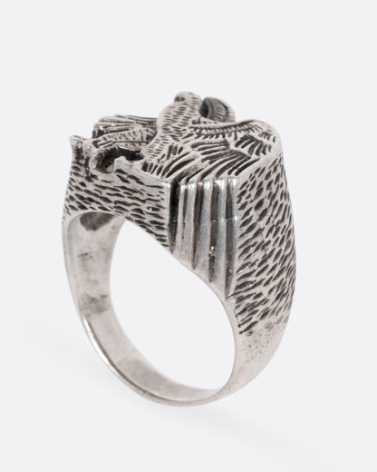 A silver signet ring with a textured eagle design, shown from the side standing up.