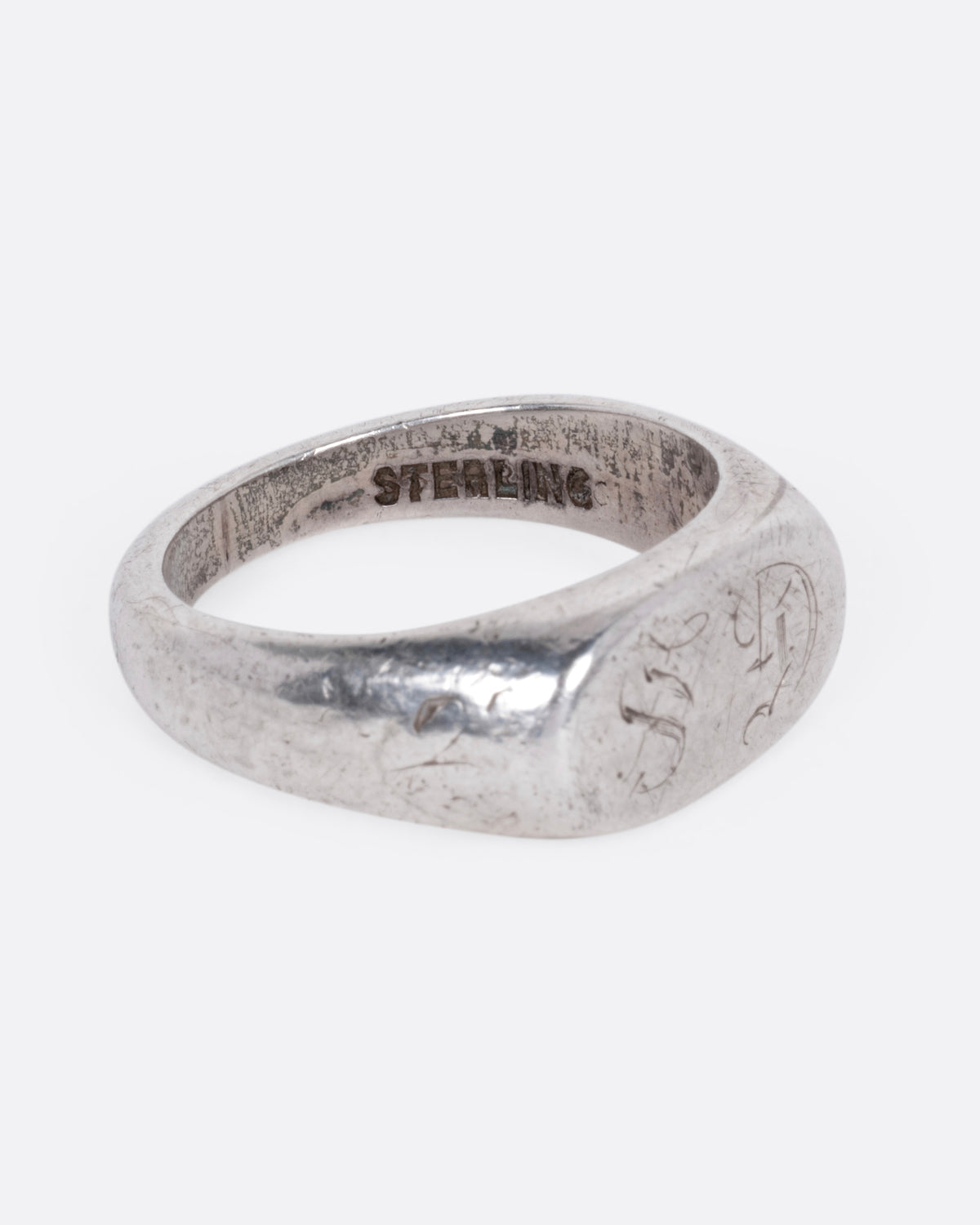 A silver signet ring with a faint engraving of 'GS' on its broad face, shown from the side.