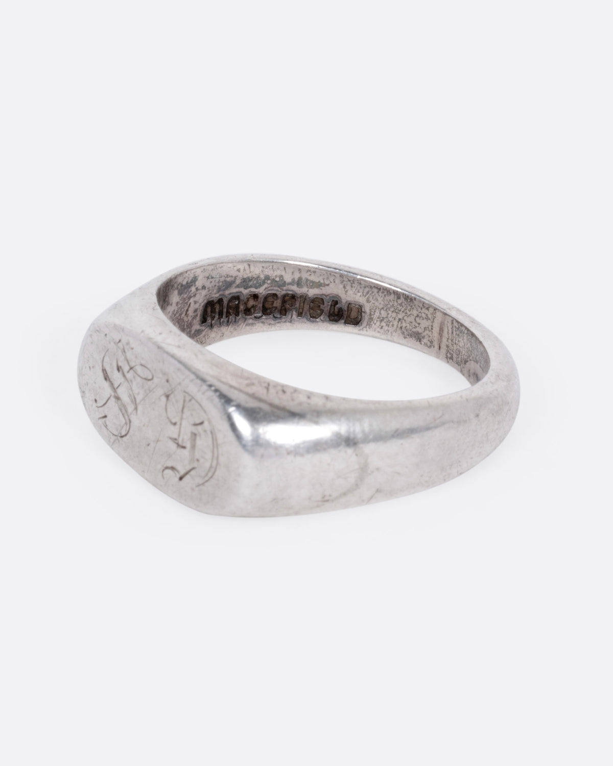 A silver signet ring with a faint engraving of 'GS' on its broad face, shown from the side.