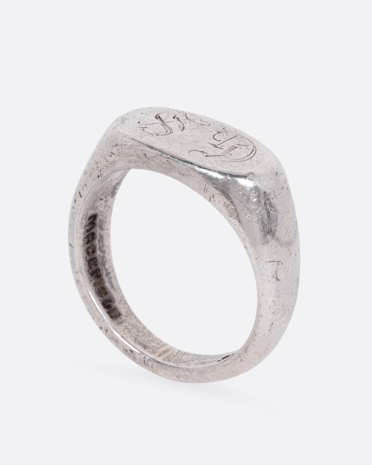 A silver signet ring with a faint engraving of 'GS' on its broad face, shown from the side standing up.