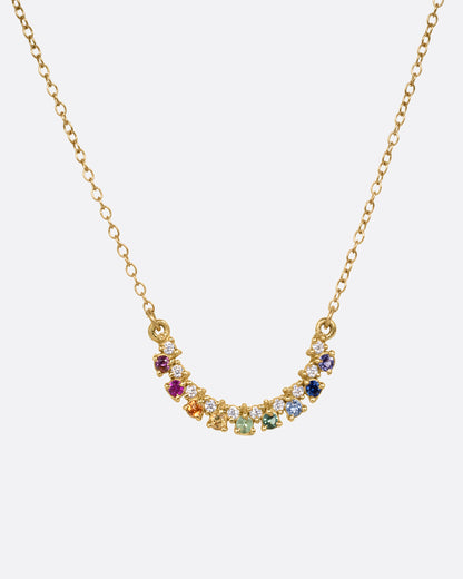 A yellow gold cable chain necklace with a crescent shaped pendant with multicolored gemstones, shown from the front.