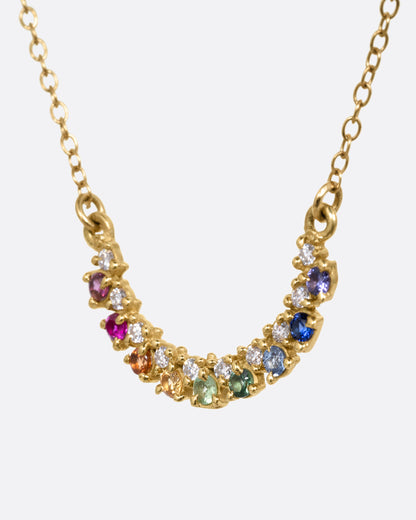 A yellow gold cable chain necklace with a crescent shaped pendant with multicolored gemstones, shown from the side.