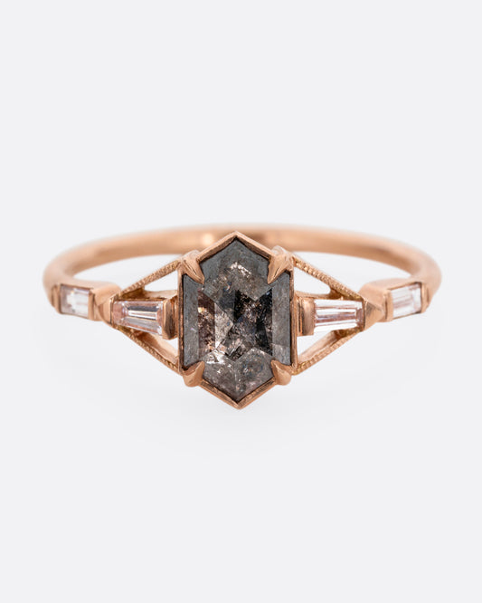A rose gold ring with a black hexagonal diamond and baguette diamond lined shoulders. Shown from the front.