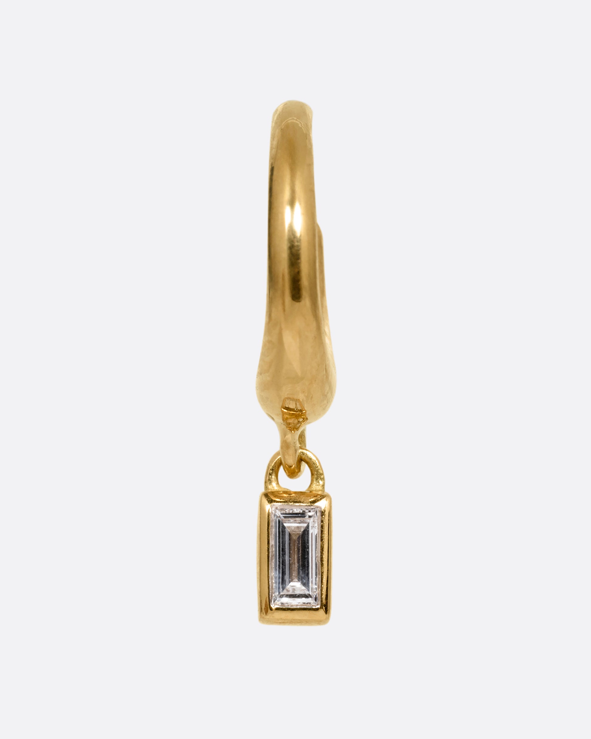 A yellow gold huggie hoop earring with a baguette diamond dangle. Shown from the front.