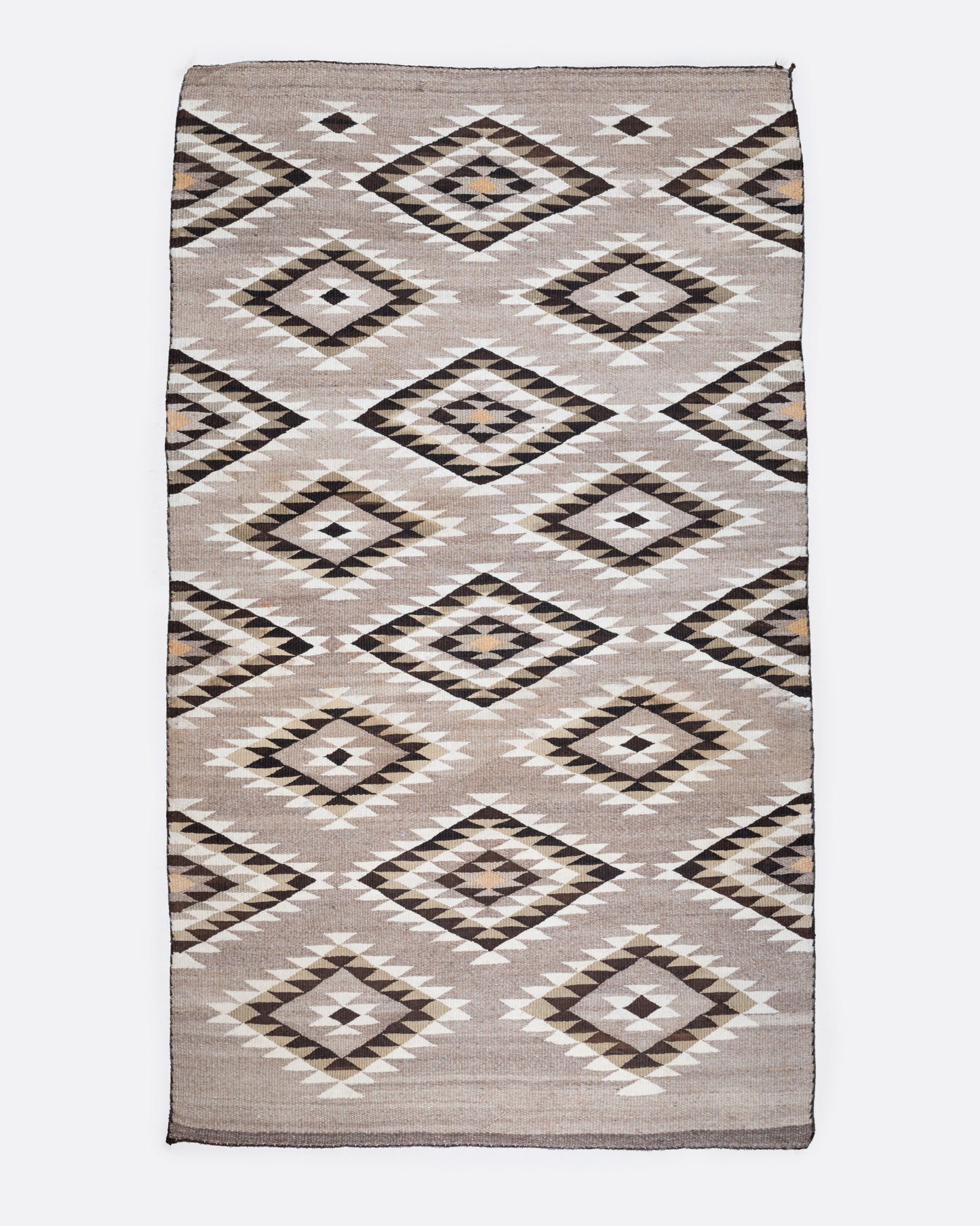 A bird's eye view of a tan, black, and white Navajo Diamond Eye Dazzler rug with a serrated diamond motif.