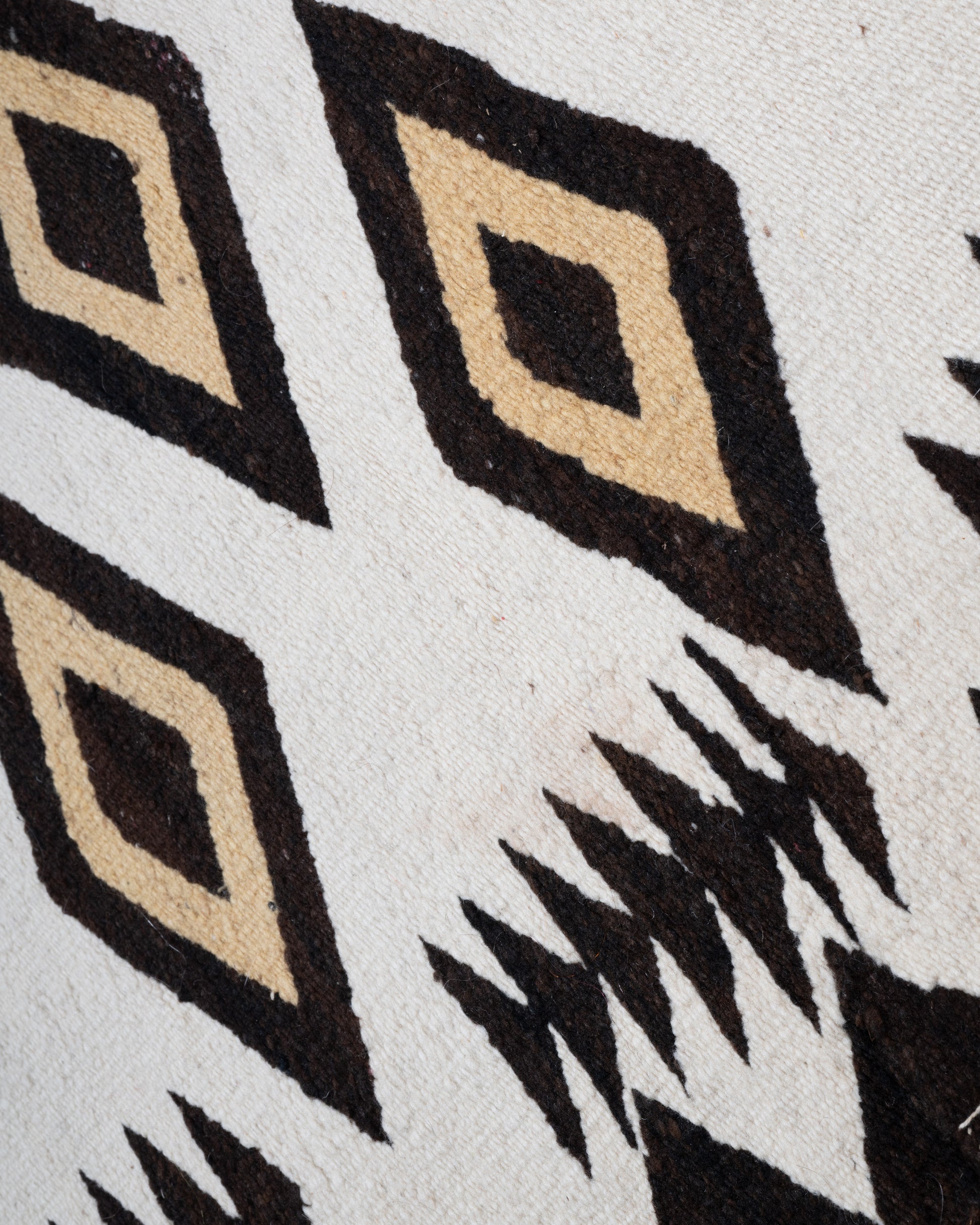 A close up of a white, black, and yellow Navajo Crystal weaving rug with a bold border and stacked diamond pattern.