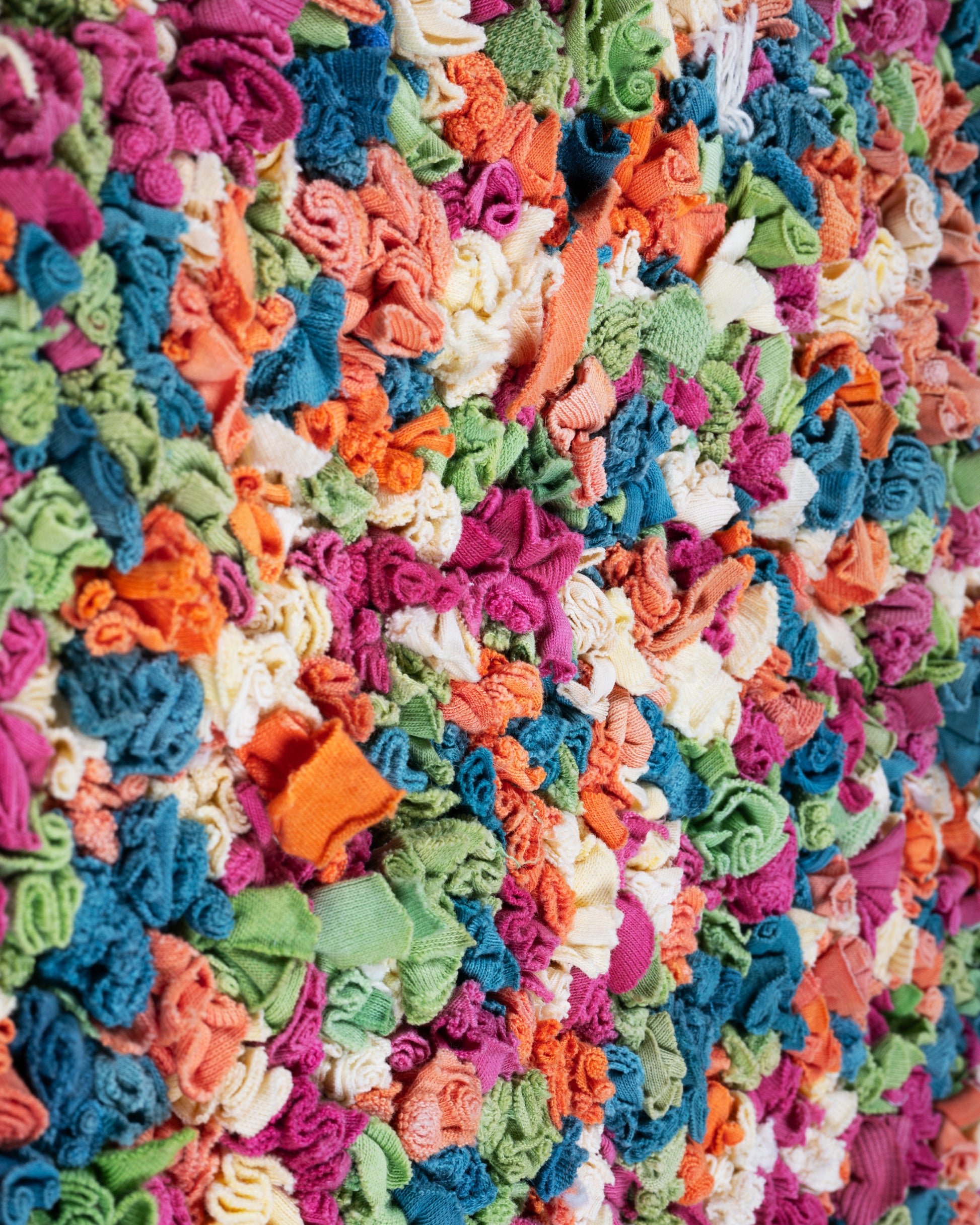 A close up of  green, red, orange, and white rectangular rag rug.