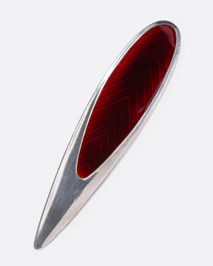 A silver and red enamel pin with a chevron pattern, shown from the front.