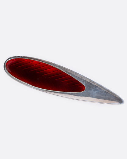 A silver and red enamel pin with a chevron pattern, shown from the front.