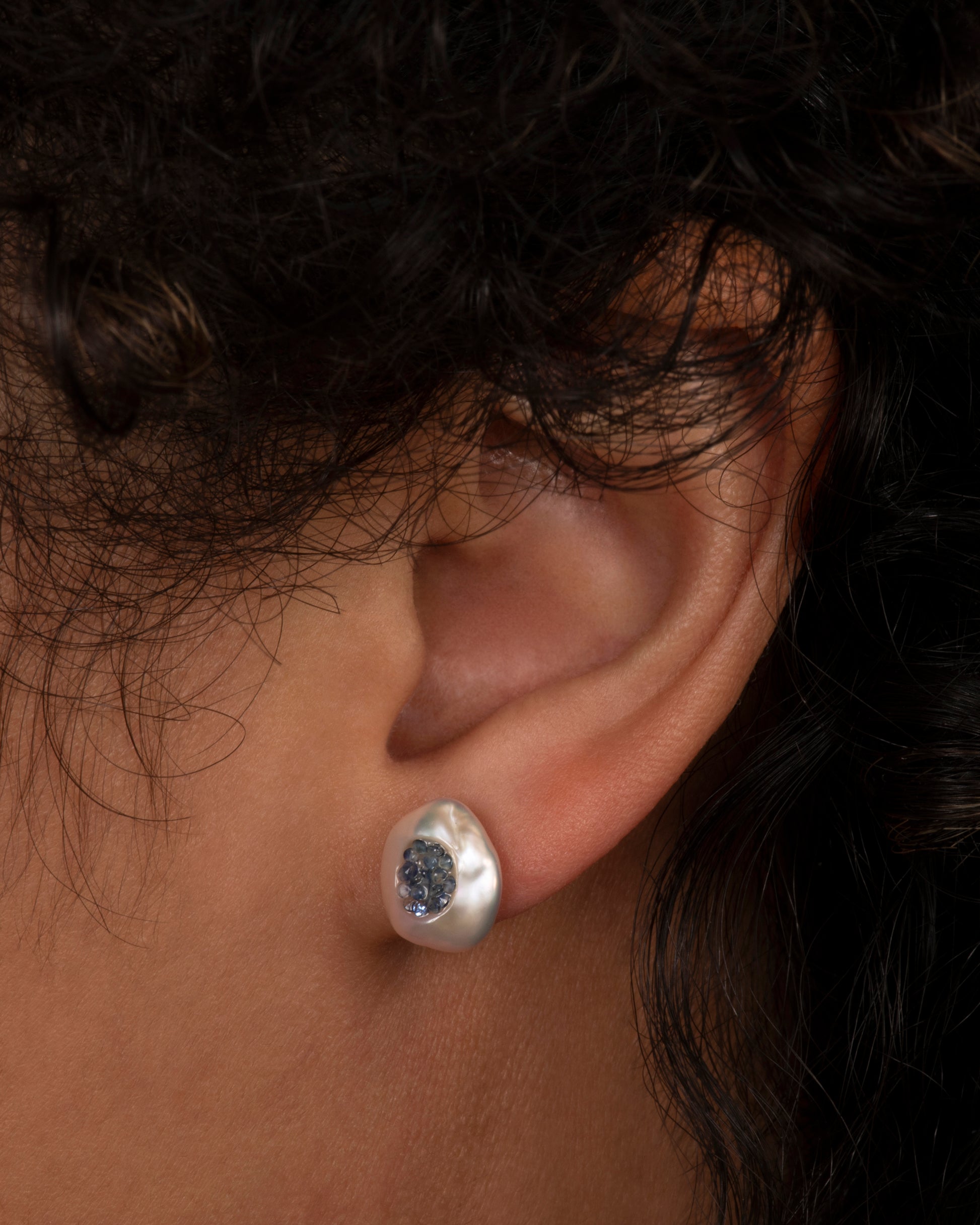 A pair of yellow gold earrings with hollowed out pearls filled with sapphires. Shown on an ear.