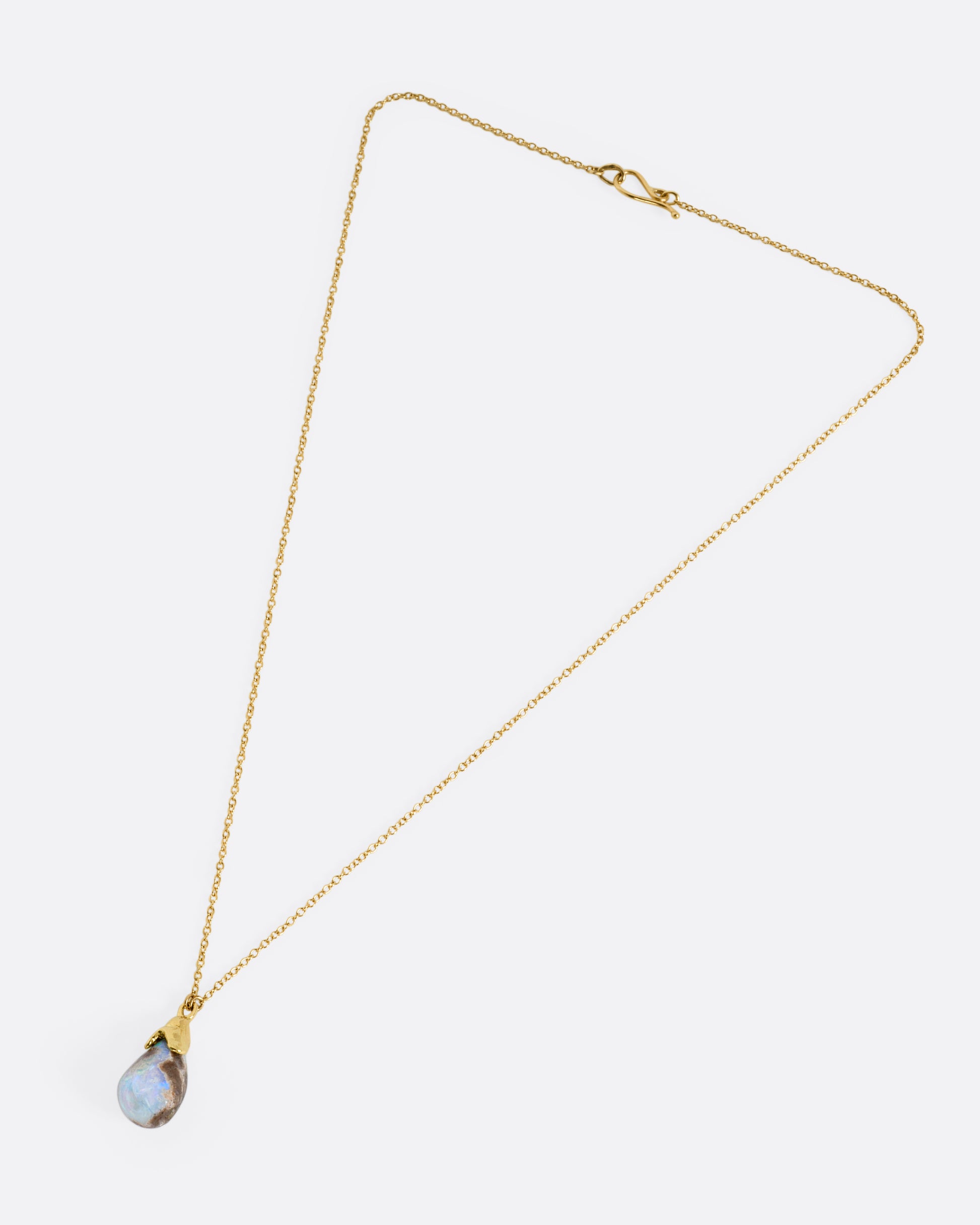 A yellow gold necklace with a teardrop shaped opal pendant, shown laying flat.